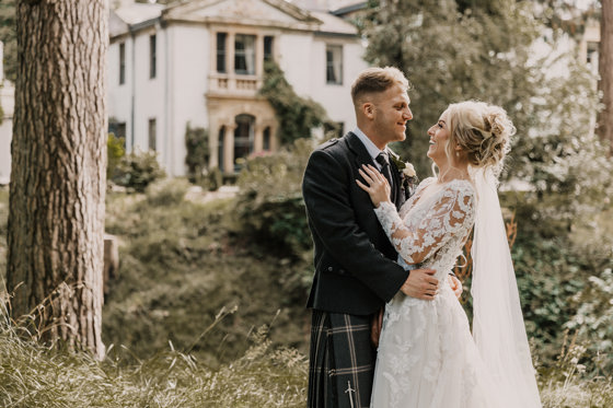 Smiling bride and groom embrace outside Norwood Hall Hotel in Aberdeen